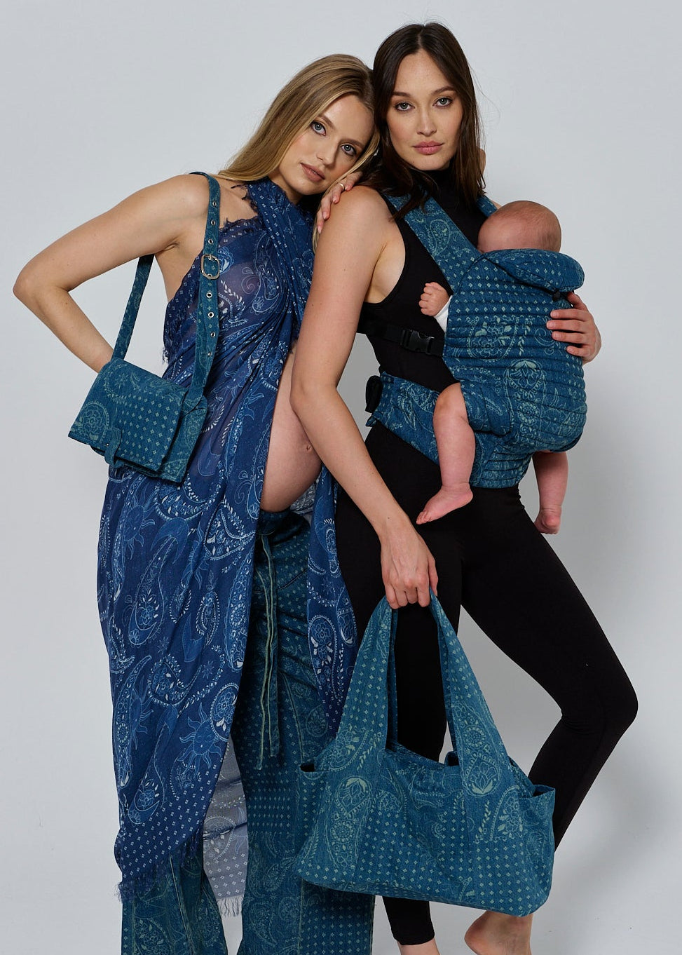 Two women holding blue denim print bags and a baby carrier with a baby inside on a white background