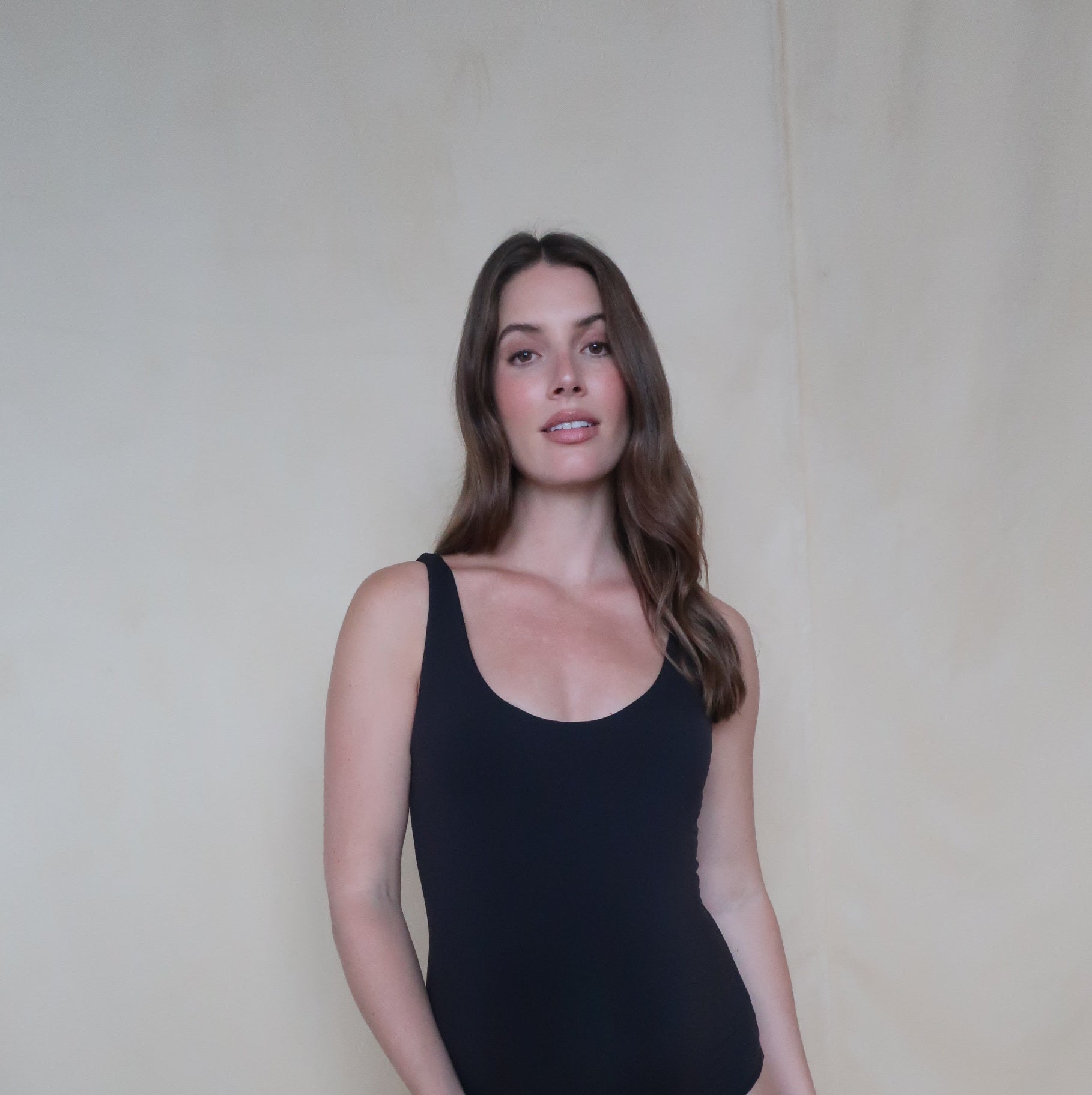 pregnant women wearing a black tank bodysuit by bumpsuit against a beige background