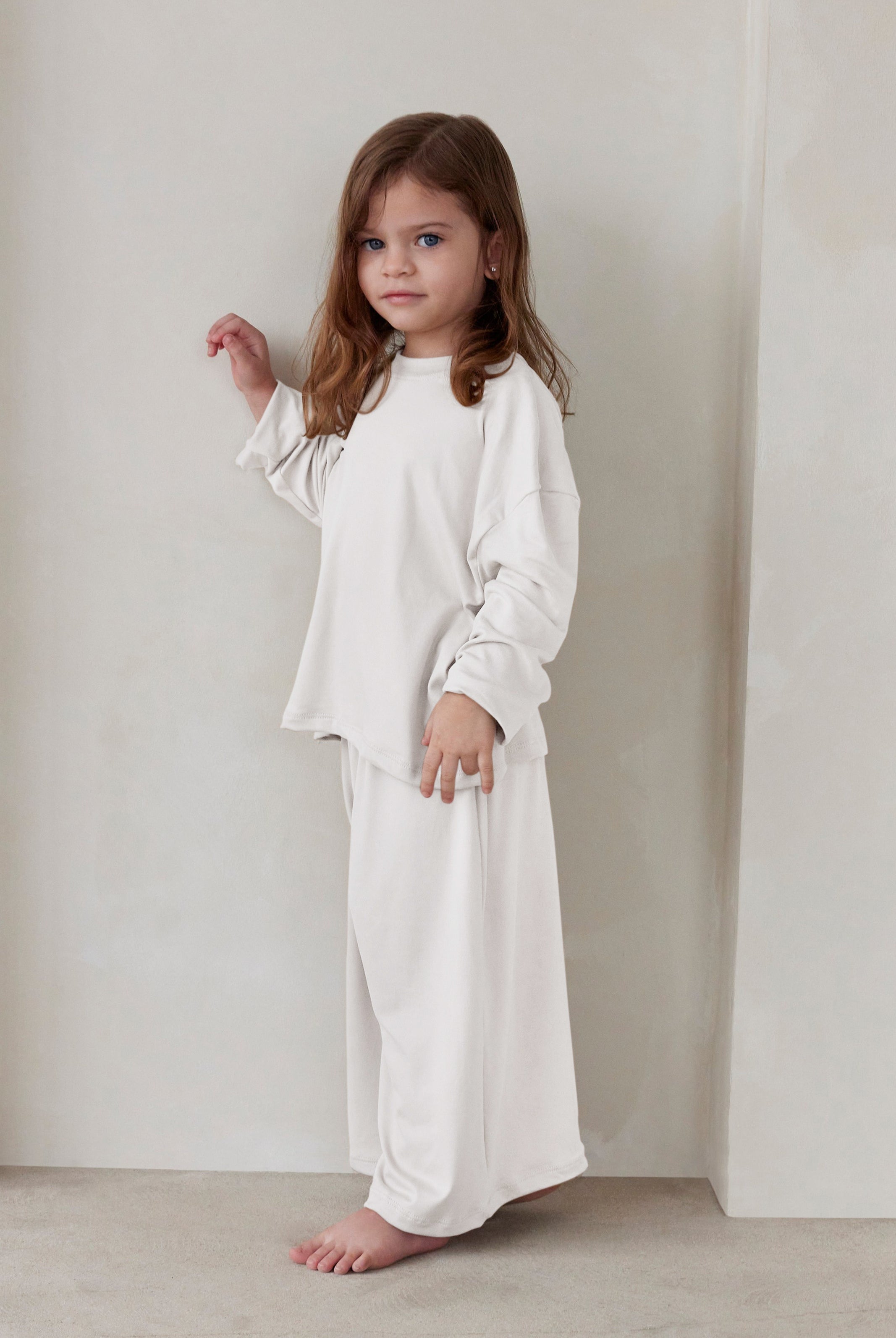 Young child wearing a white outfit standing against a plain background