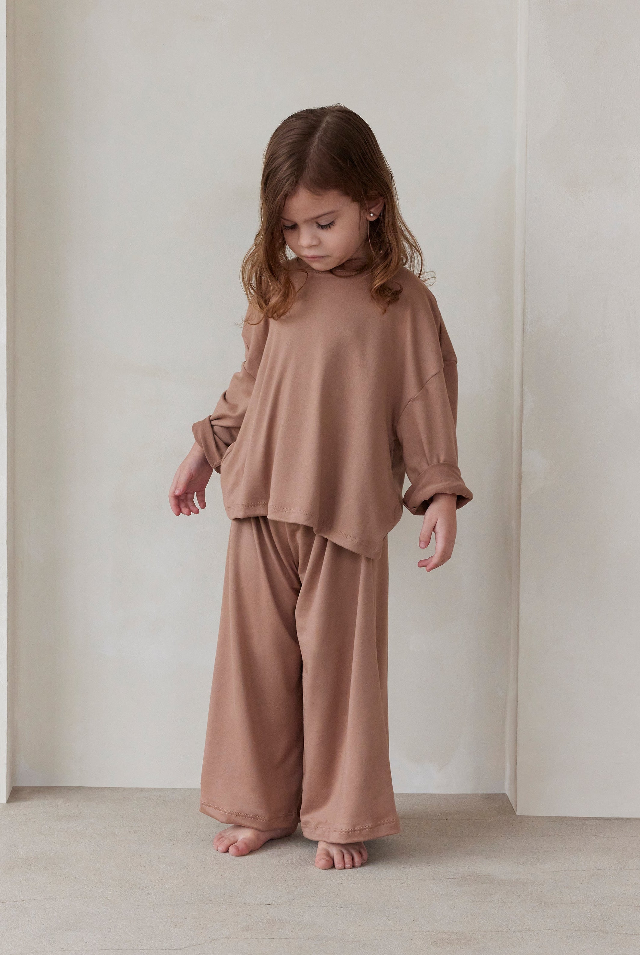 Child wearing a latte brown bumpsuit pyjamas standing against a plain background