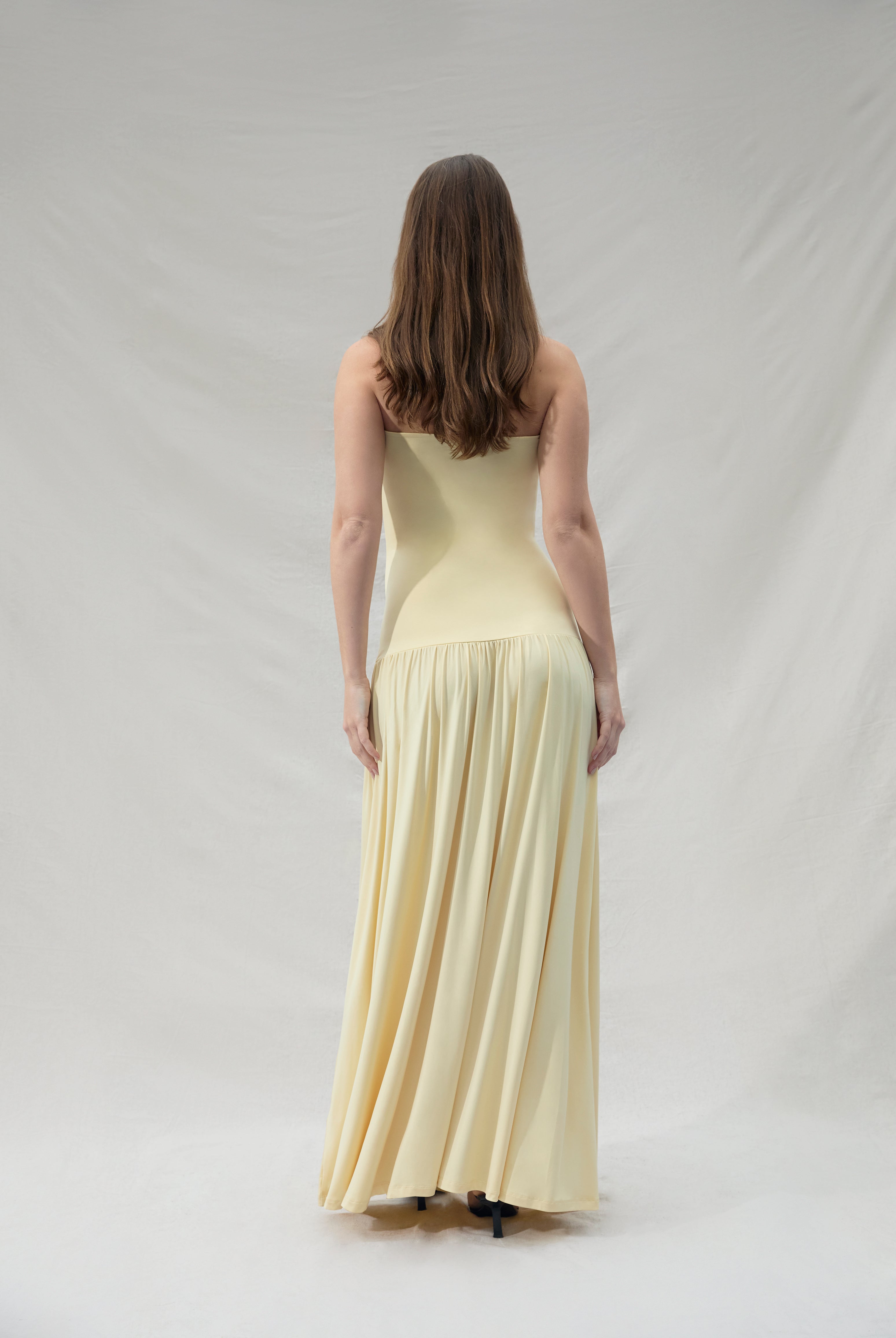 Pregnant woman wearing a maternity Bumpsuit strapless yellow dress against a plain background