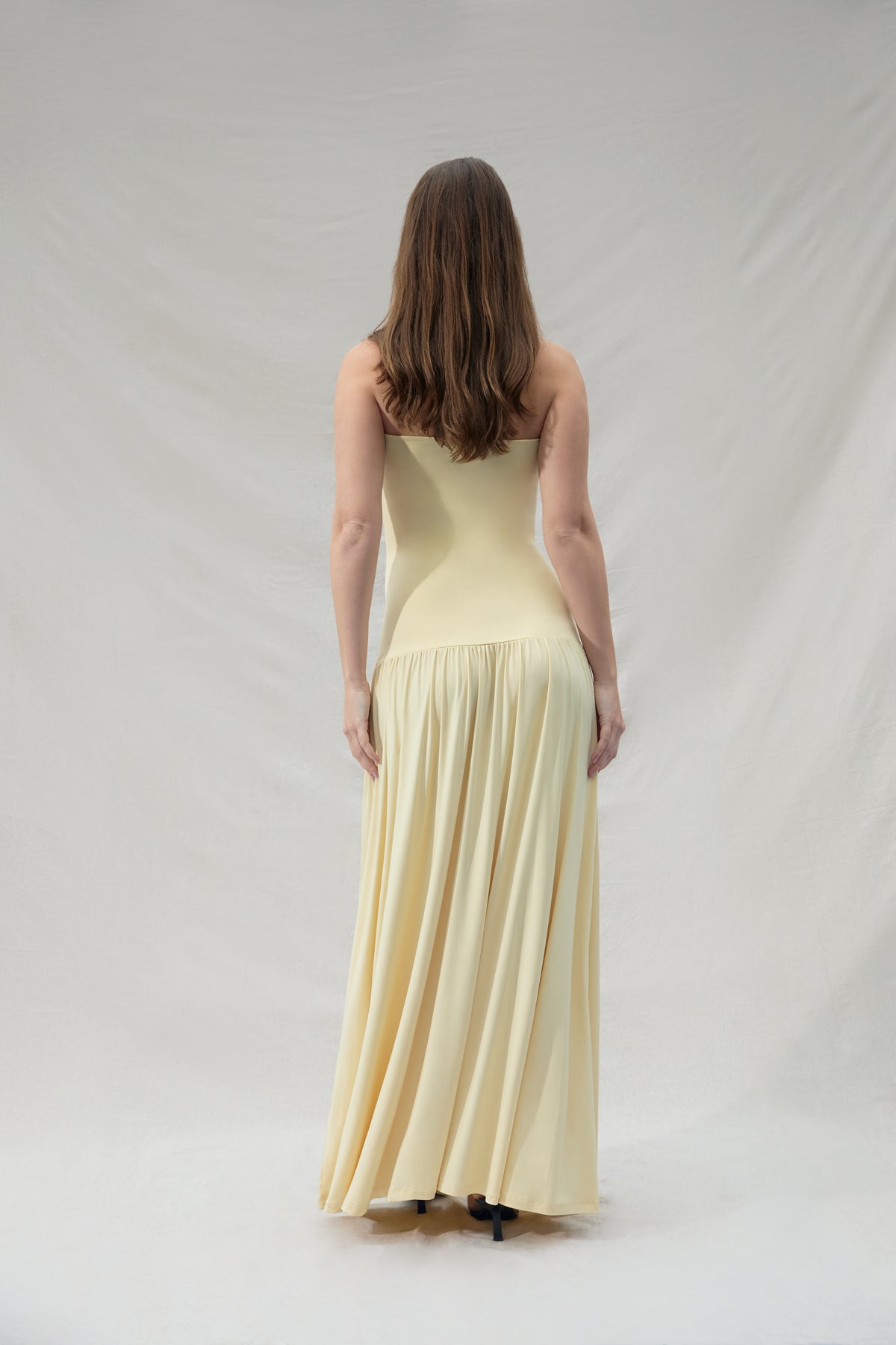 Pregnant woman wearing a maternity Bumpsuit strapless yellow dress against a plain background