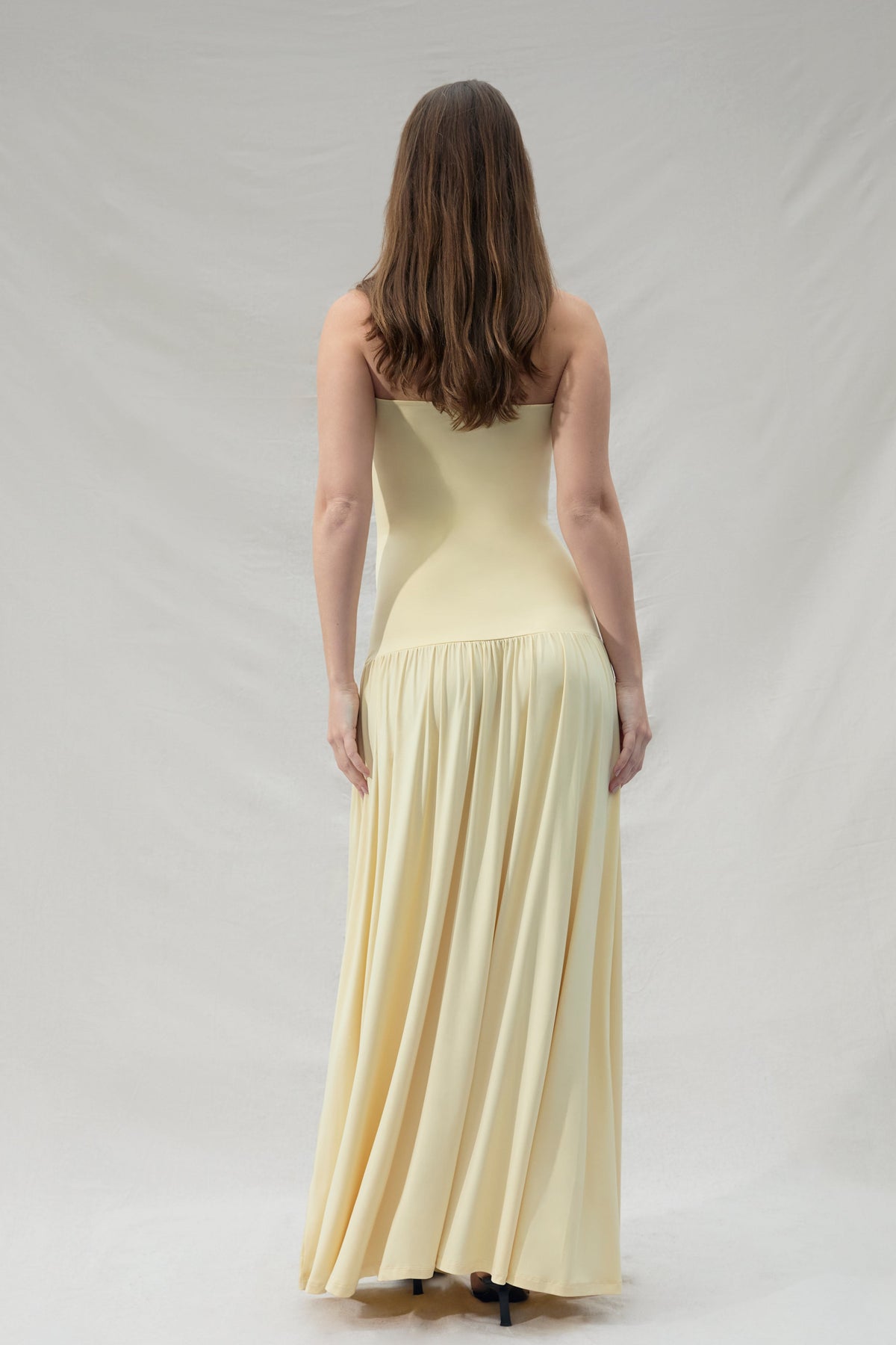Pregnant woman wearing a maternity Bumpsuit strapless yellow dress against a plain background