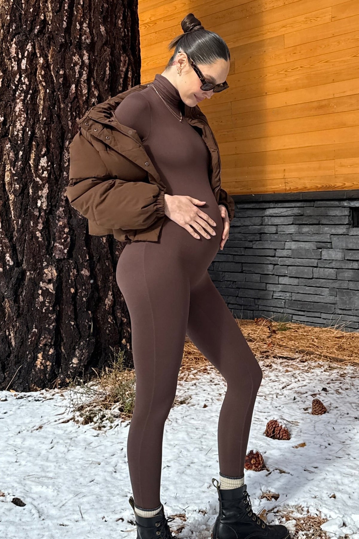 Pregnant woman wearing the penelope maternity unitard in chocolate by Bumpsuit in an outdoor winter setting