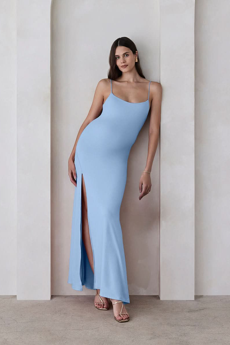 Pregnant woman wearing The Rosie maternity Square Neck Sleeveless Maxi Dress with side slit in Powder blue by Bumpsuit, standing beige against a feature wall