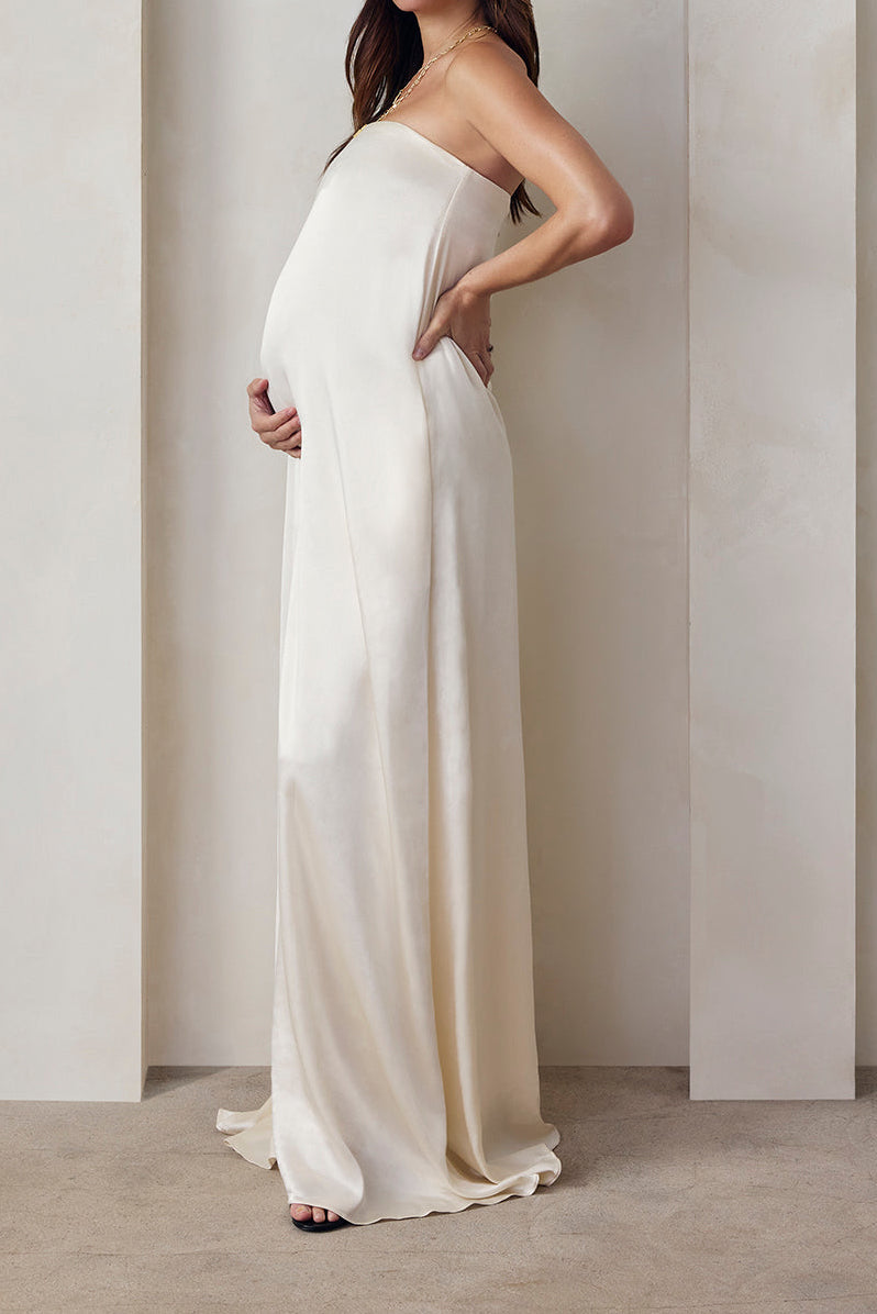 Pregnant model wearing the Bumpsuit brushed satin gown in ivory against a beige feature wall.