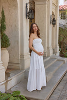 A pregnant woman wearing a white strapless shirred gown standing in a doorway.