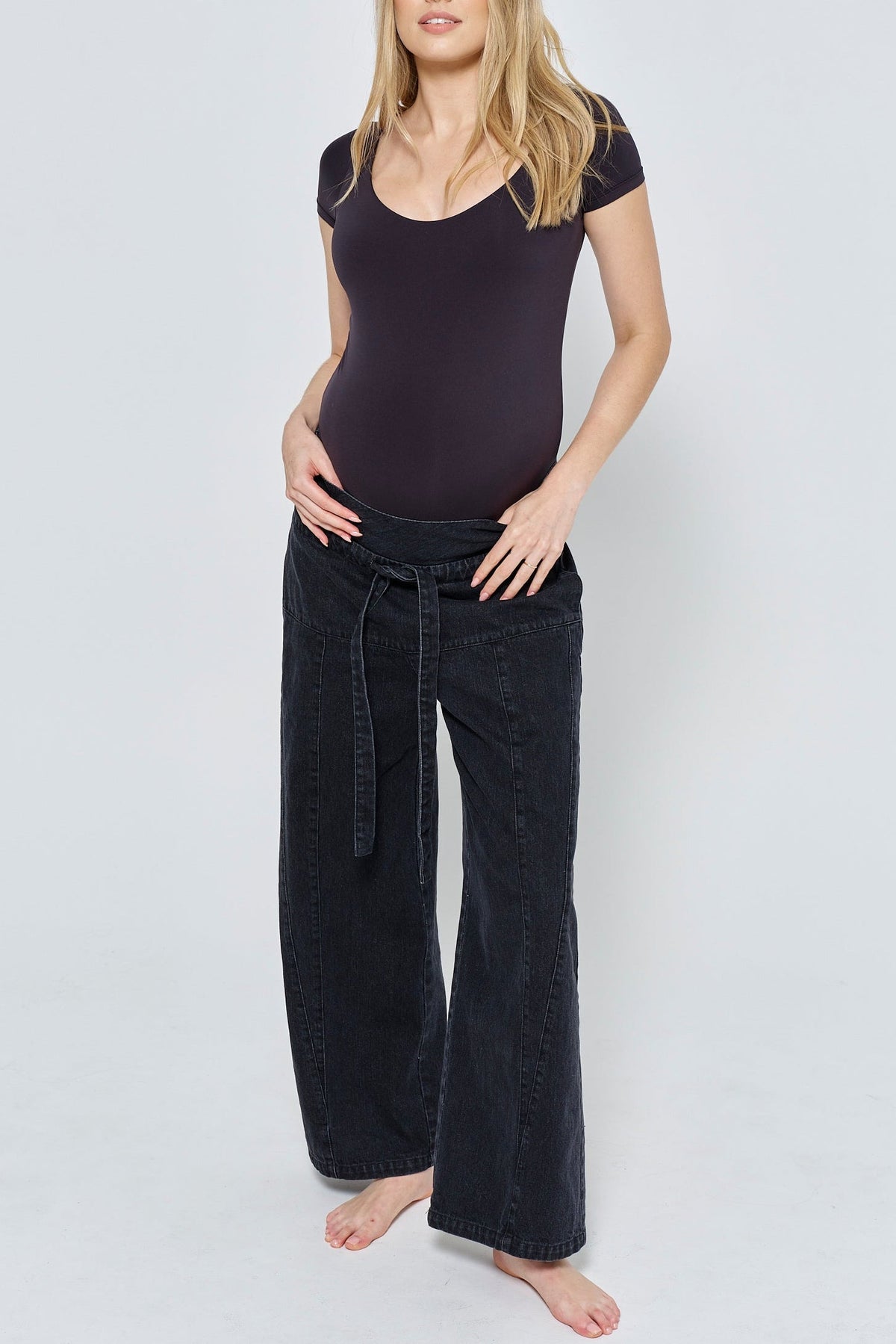 Front view of The Relaxed Denim Jean showcasing wide legs and drawstring waist on a pregnant model against a gray background