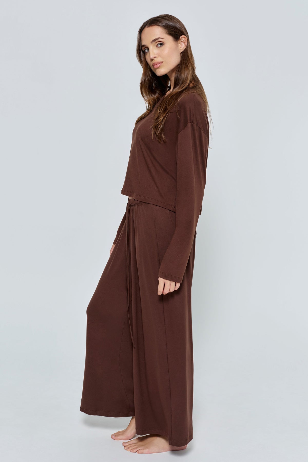 Side view of the brown Cloud Pant on a model, showcasing its wide-leg fit against a light gray background