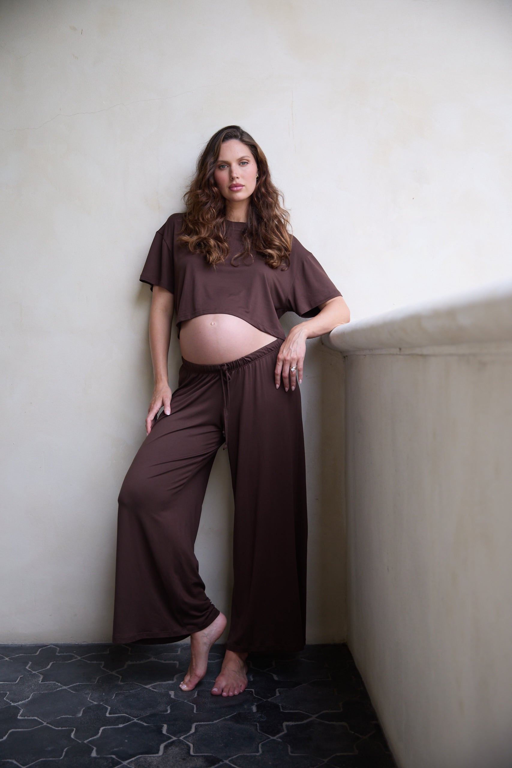 Woman in brown outfit standing against a plain wall.