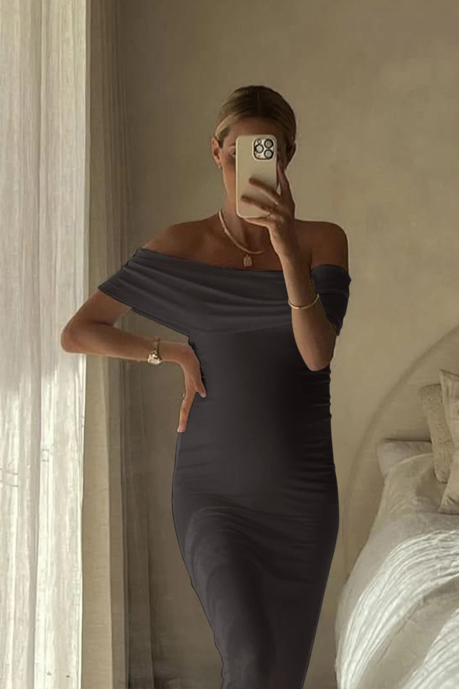 Pregnant woman taking a mirror selfie wearing an off-shoulder grey Bumpsuit dress in a bedroom.