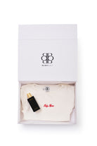 gift set with white baby mama top and black body oil bottle in a branded box on a white background