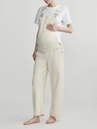 Pregnant woman wearing beige overalls on a plain background
