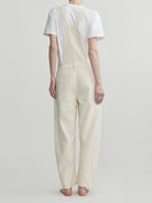 Person wearing cream-colored overalls and a white t-shirt on a plain background