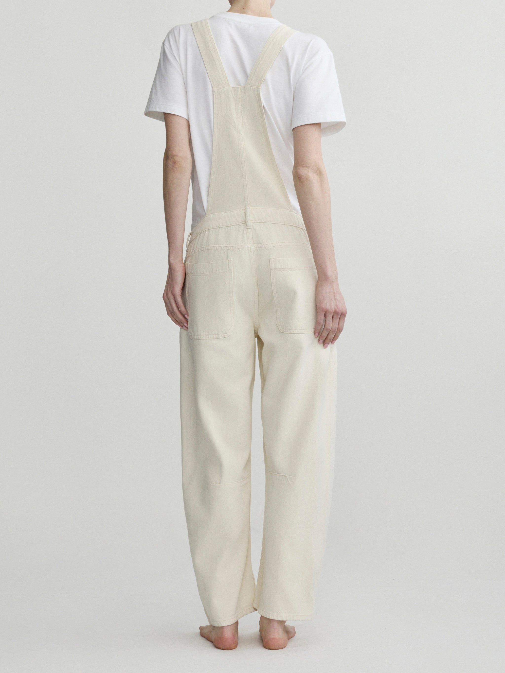 Person wearing cream-colored overalls and a white t-shirt on a plain background
