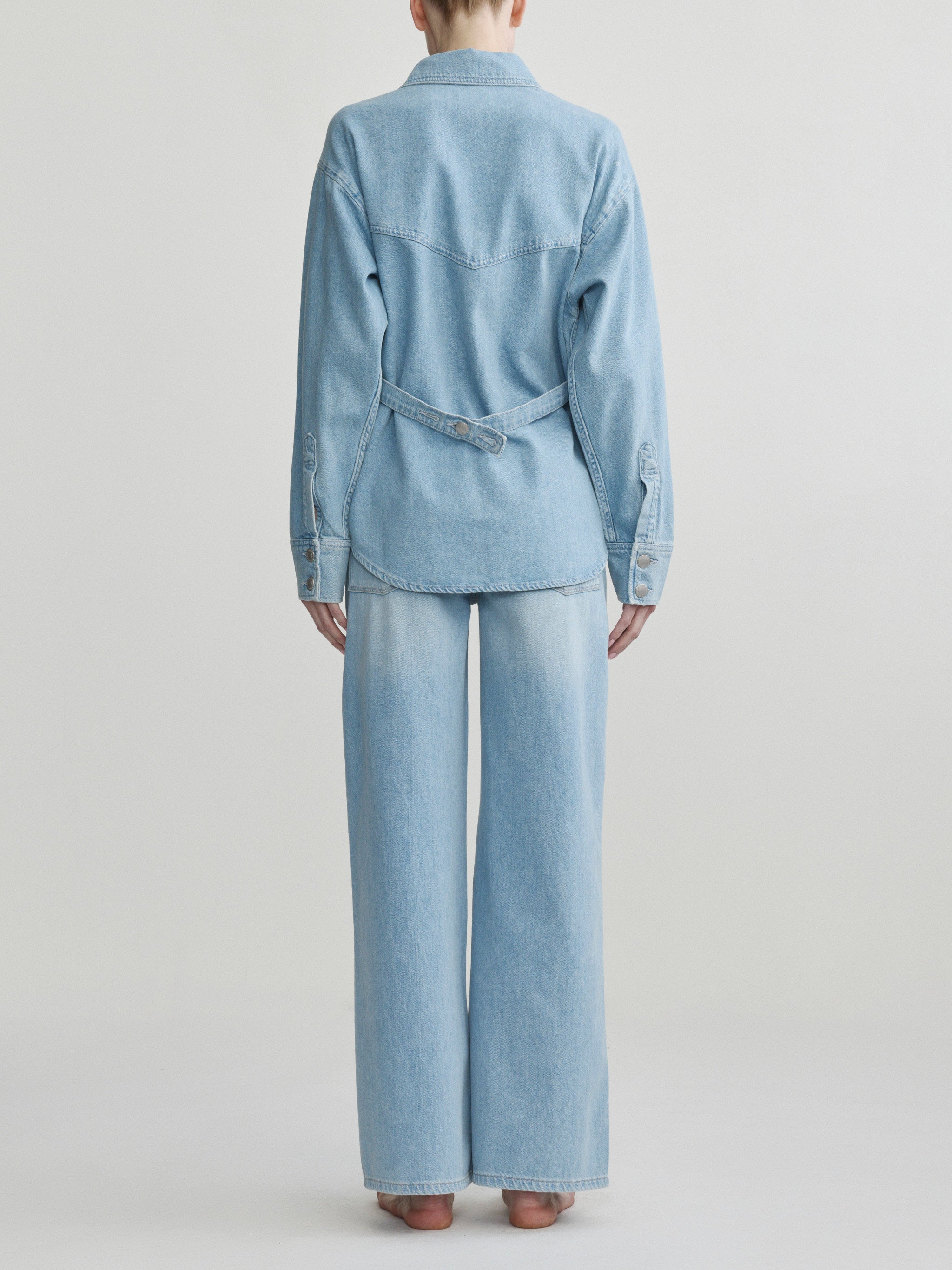 Person wearing a light blue denim outfit on a plain background