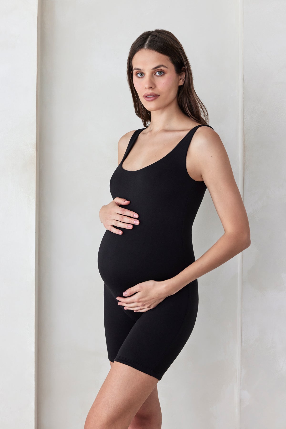 Pregnant woman wearing a black sleeveless Cindy romper against a white background