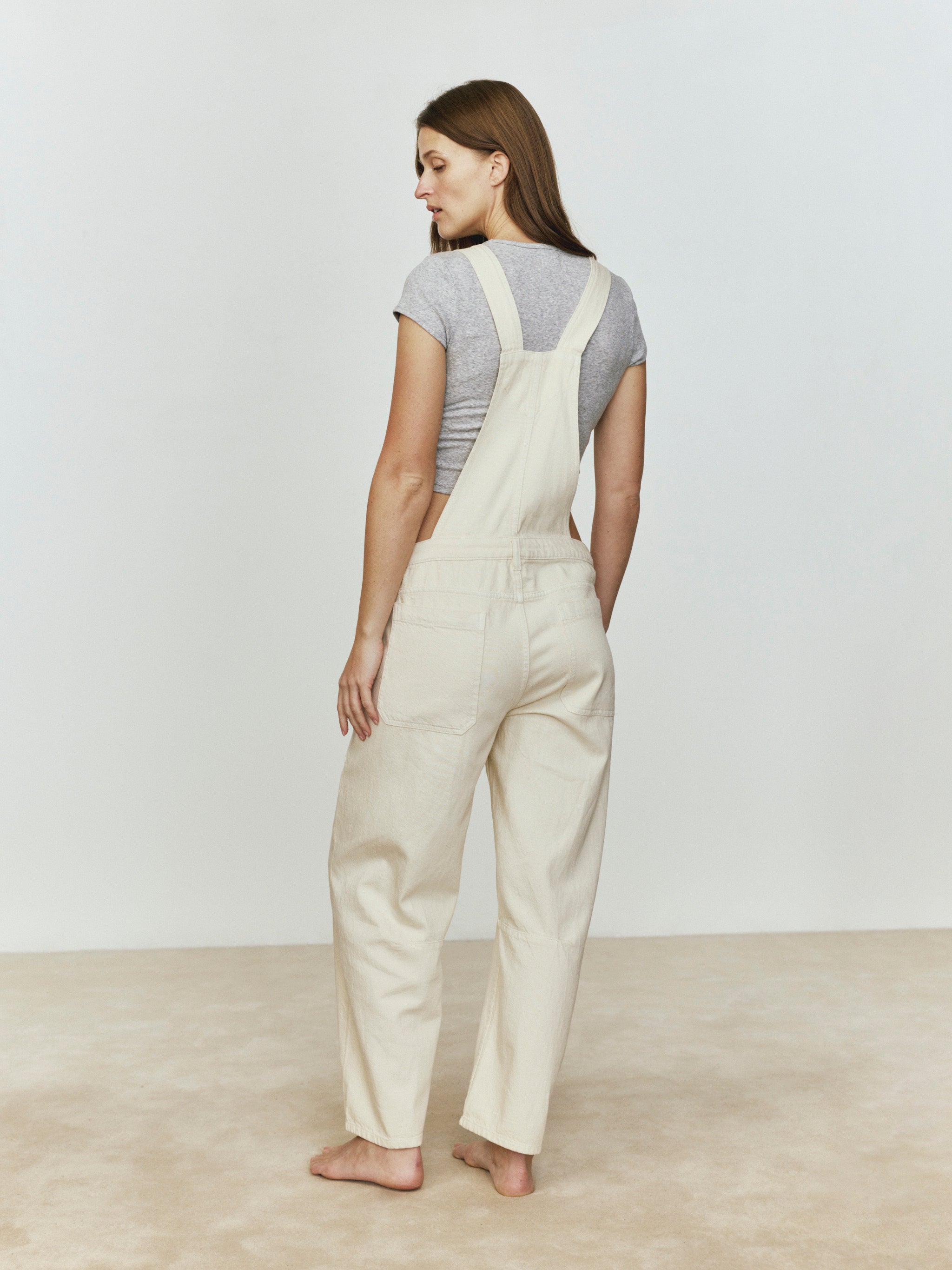 Woman wearing beige overalls against a plain background