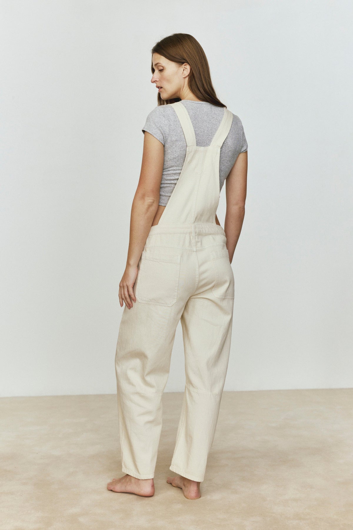 Woman wearing beige overalls against a plain background