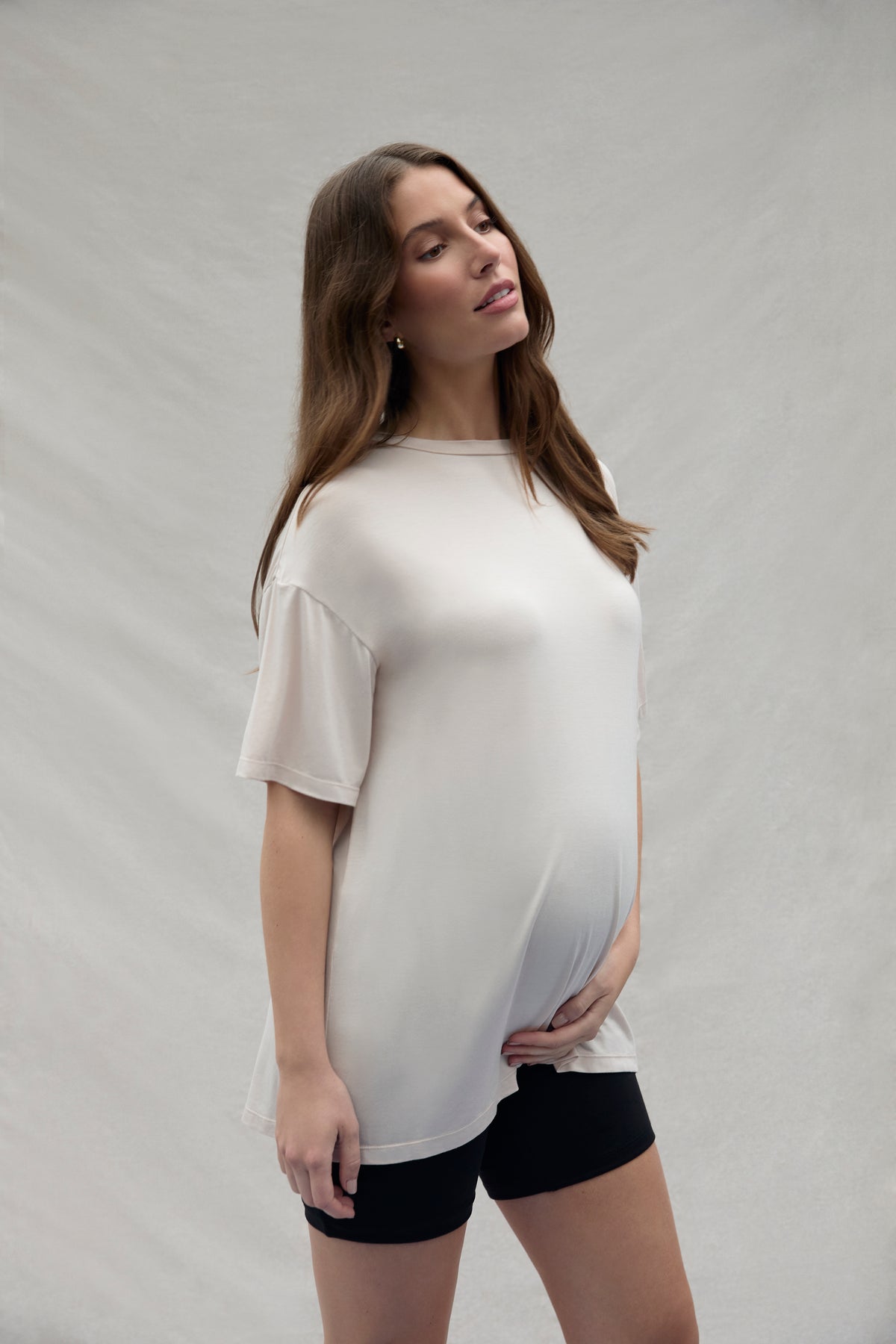 Woman wearing a soft oat colored t-shirt and black shorts on a plain background
