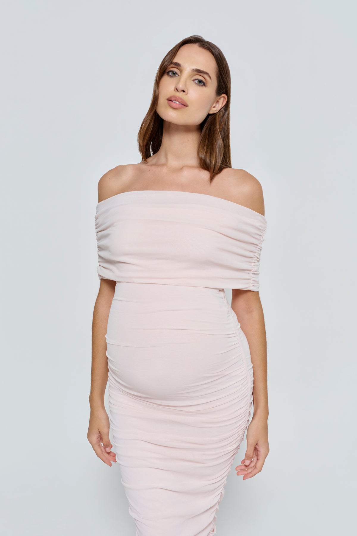 Woman wearing a light pink mesh off-shoulder dress against a white background