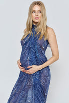 Pregnant woman wearing a blue patterned scarf dress against a white background