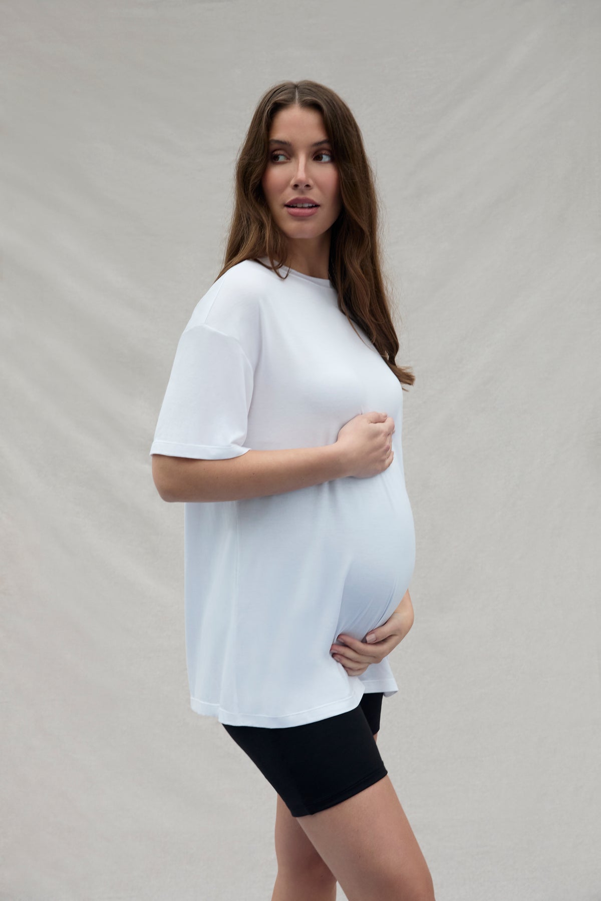 Woman wearing a white t-shirt and black shorts against a plain background