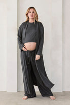 Woman wearing a dark grey slate Bumpsuit Cloud outfit standing in a minimalistic room with beige walls and arches.