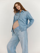 Pregnant woman wearing a light blue denim jacket and jeans on a plain background