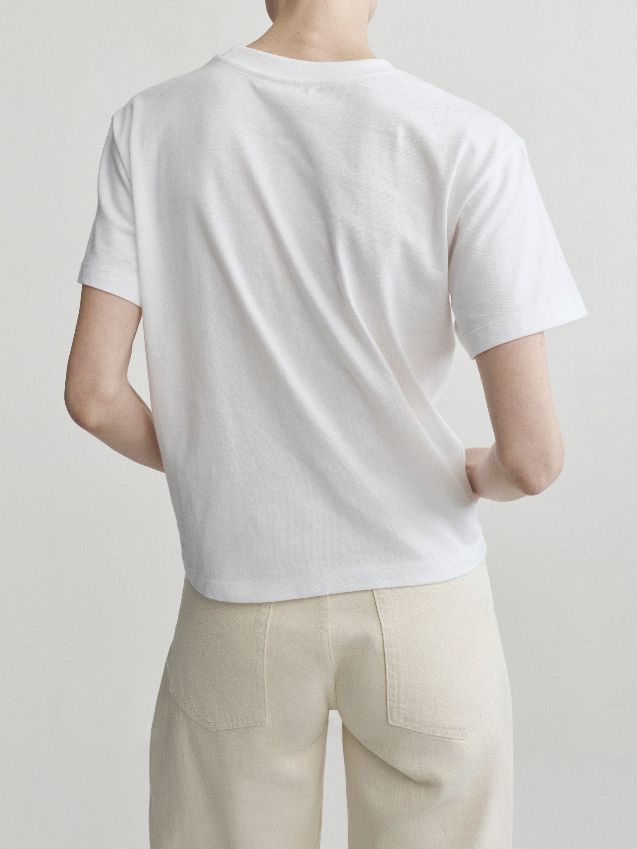 Person wearing a plain white t-shirt and beige pants on a light gray background