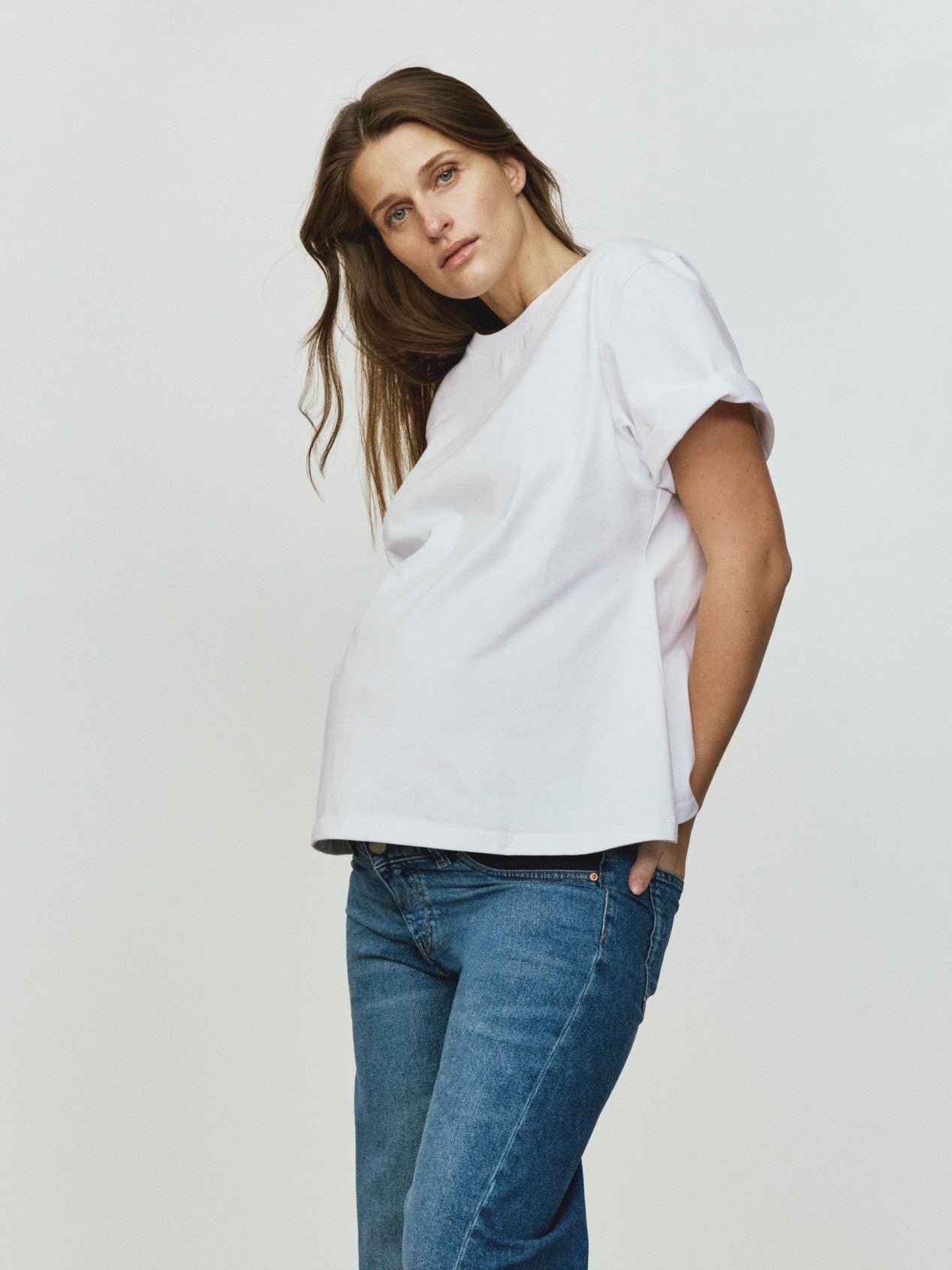 Woman wearing a white top and blue jeans standing against a plain background