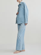 Pregnant woman wearing a light blue denim outfit on a plain background