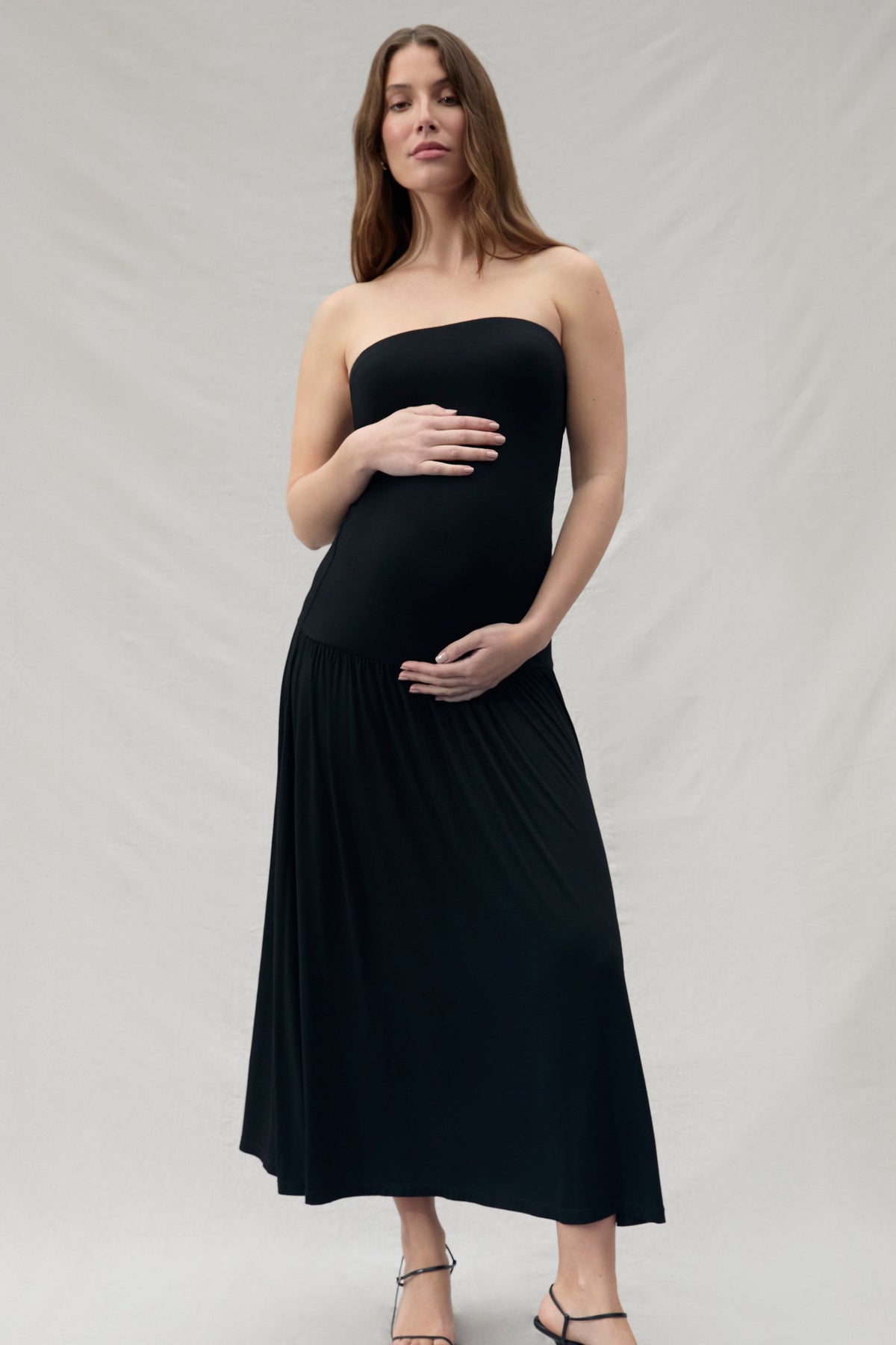 Pregnant woman wearing a black strapless dress on a plain background