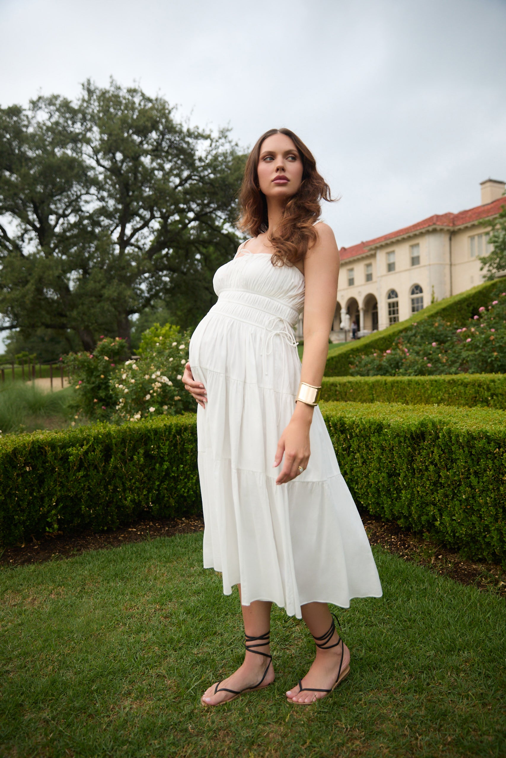 Pregnant woman in a white dress standing in a garden.