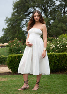 Woman in a white strapless dress standing outdoors with greenery in the background