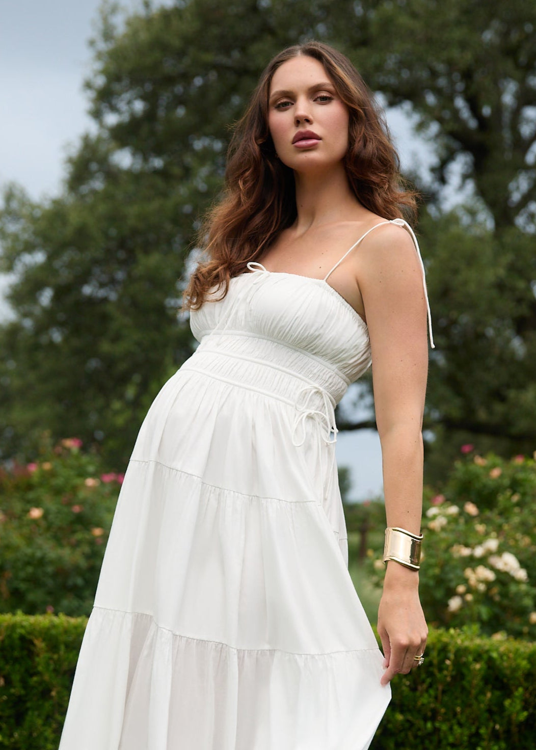 Woman in a white dress standing outdoors with greenery in the background