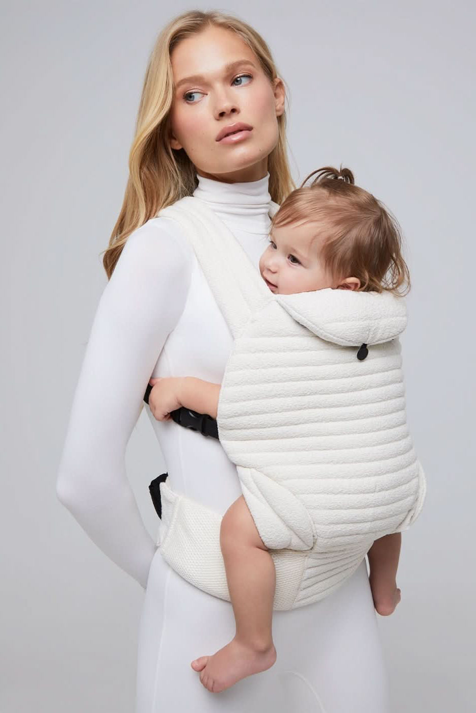 Model wearing an ivory coloured baby carrier with white background in bumpsuit one piece