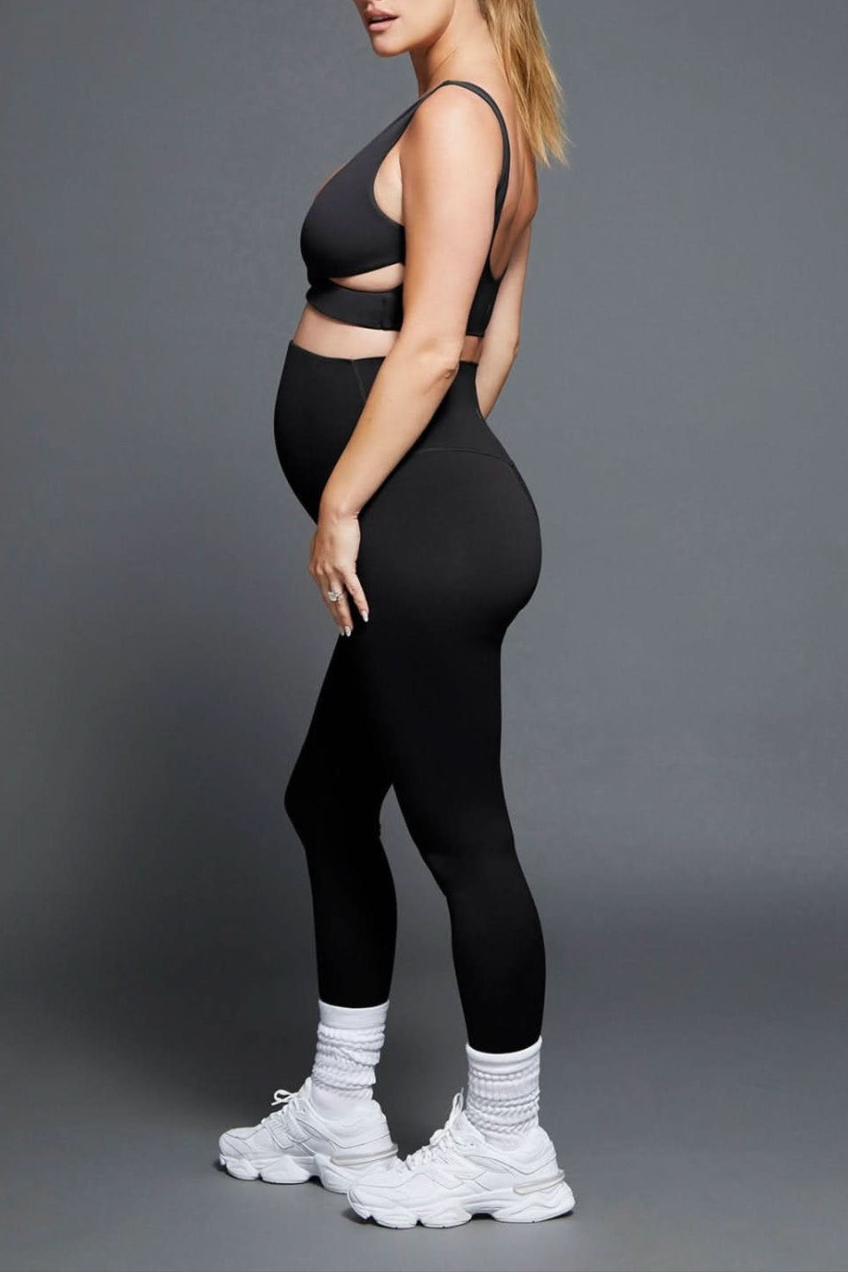 Side view of black The Perfect Movement Maternity Legging showing its maternity fit on a model against a gray background
