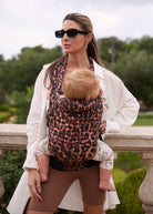 Woman holding a baby in a leopard print baby carrier outdoors