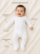 Baby wearing a white convertible babysuit on a beige blanket with feature labels.