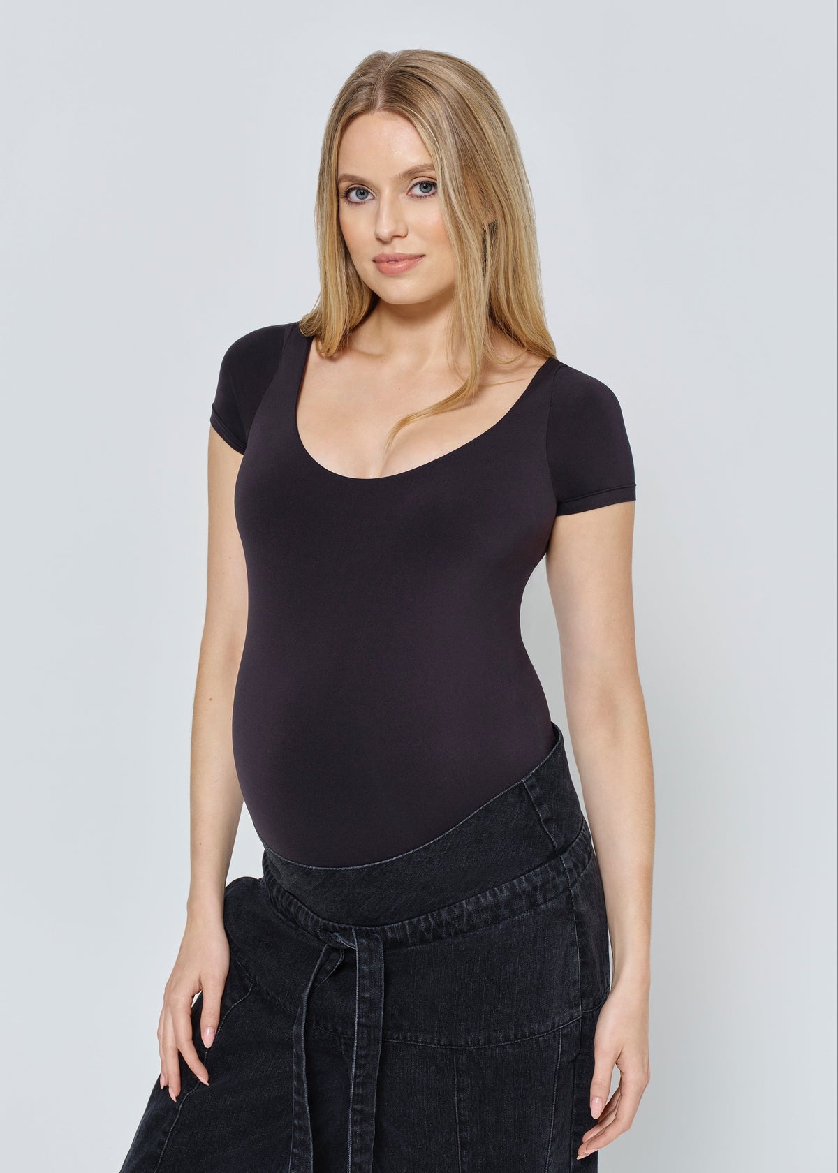 Woman wearing a black scoop scoopneck bodysuit against a light gray background