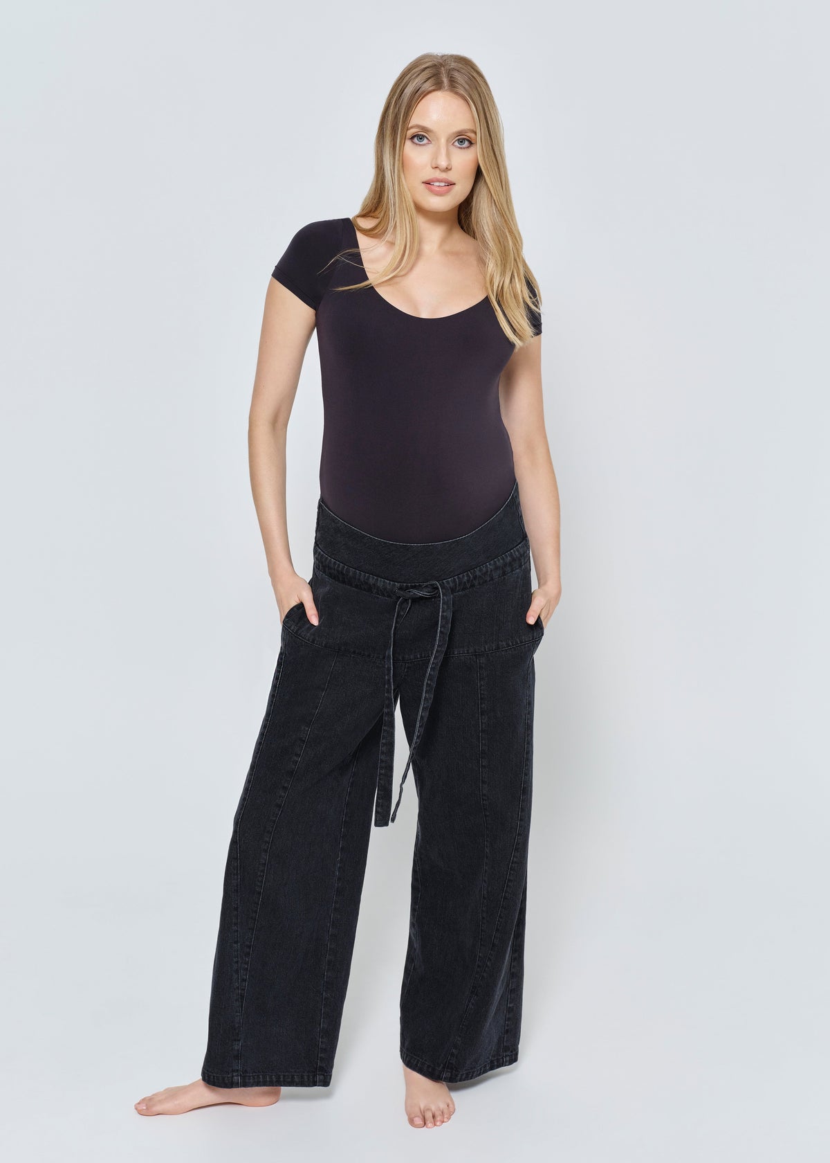 Pregnant woman wearing a black outfit with wide-leg pants on a white background