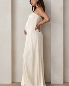 Side view of a pregnant woman wearing a Bumpsuit brushed satin gown in champagne color 