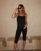 Pregnant woman wearing a black Bumpsuit camisole tank top and capri leggings against a beige wall