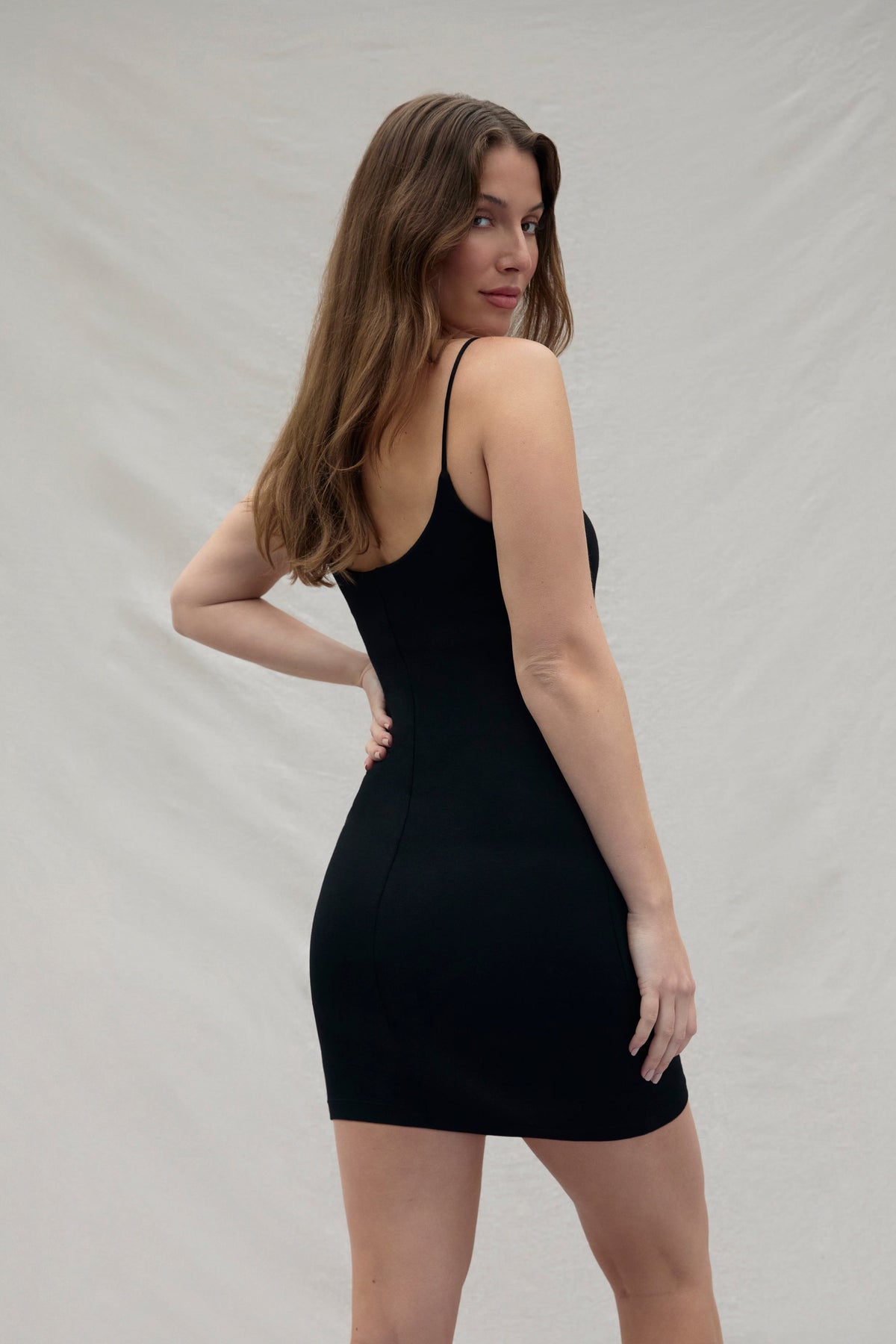 Back view of a woman wearing a cotton mini black dress against a plain background