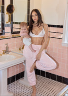 Woman holding a baby in a bathroom with pink tiles and a sink.