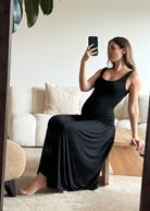 Woman in a black dress taking a mirror selfie in a living room.