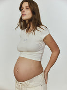 Pregnant woman wearing a white t-shirt and pants against a plain background