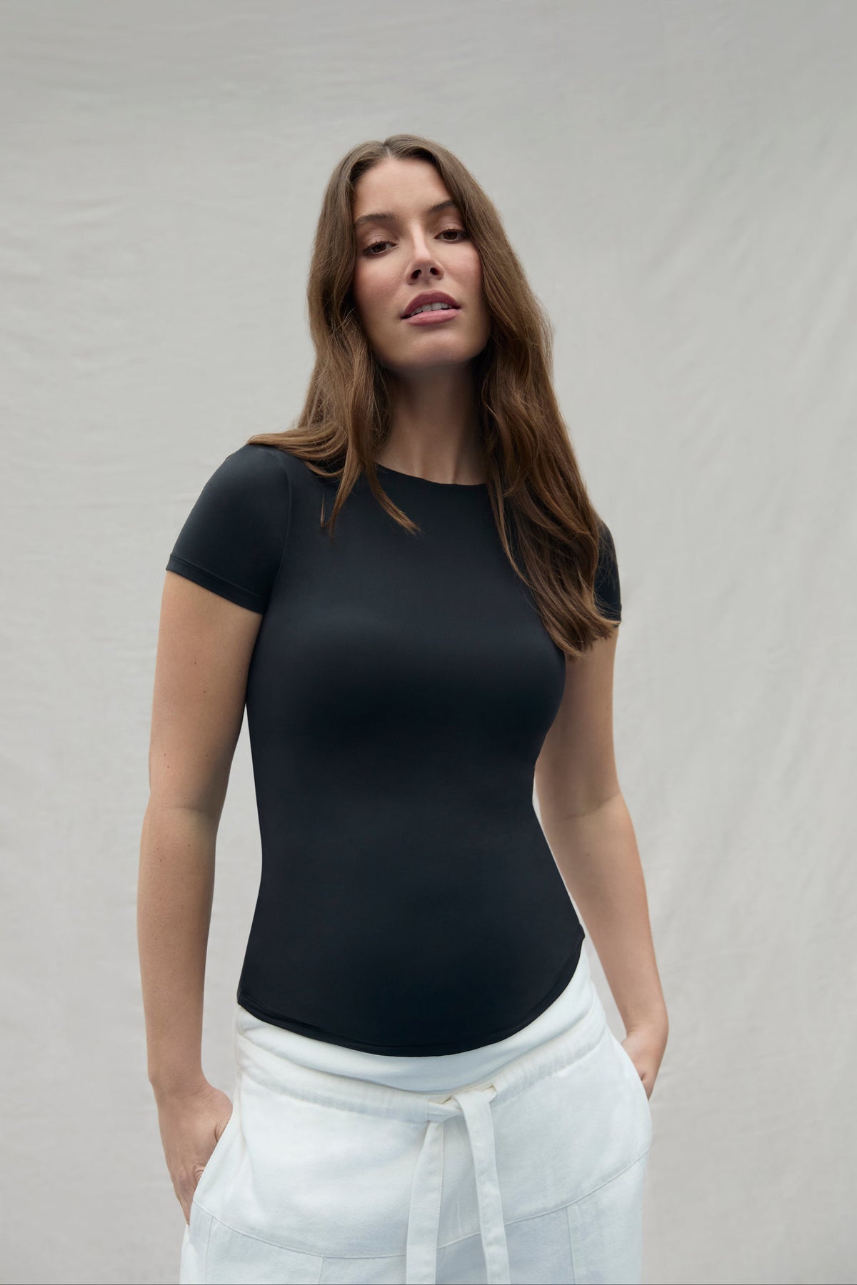 Woman wearing a black t-shirt and white pants against a plain background