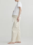 pregnant person wearing a white t-shirt and beige pants on a plain background